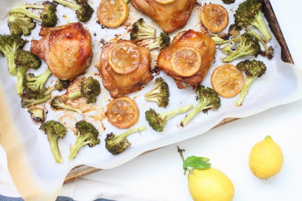 A sheet pan with roasted soy sauce chicken thighs and broccoli garnished with lemon