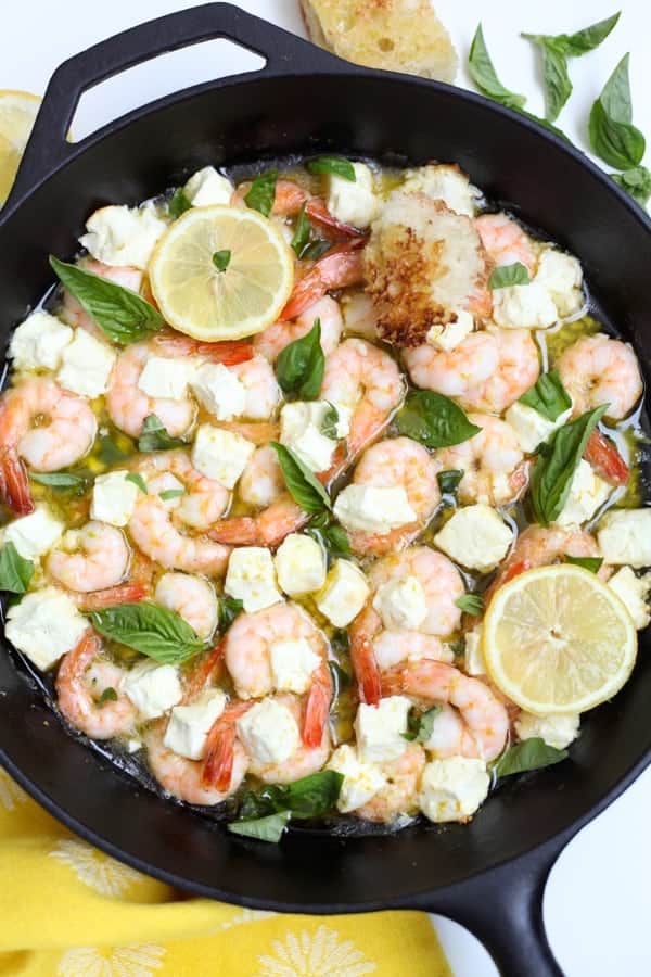 Black cast iron skillet with roasted shrimp, feta, olive oil and garlic with fresh basil