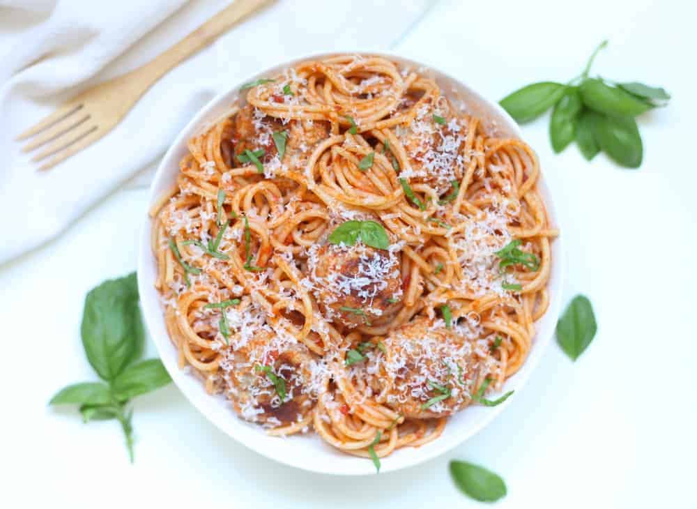 A white bowl filled with spaghetti, meatballs and red sauce