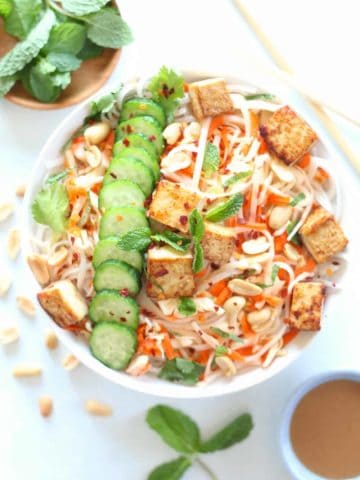 White bowl filled with rice noodles, raw cabbage and carrots, tofu and peanut lime dressing