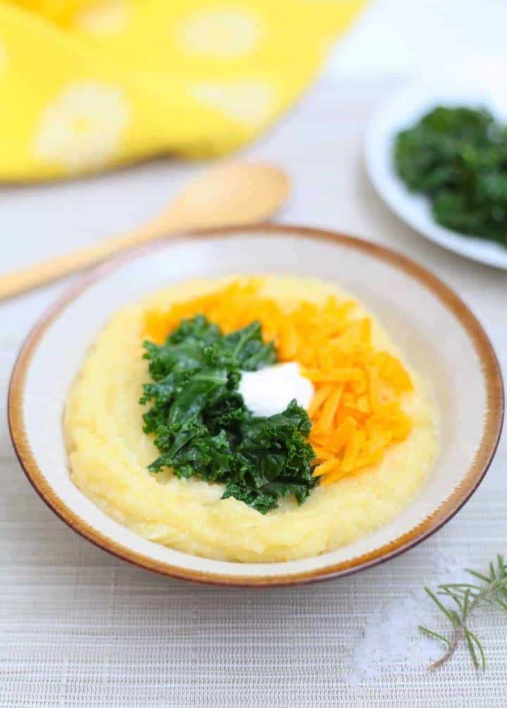 Bowl filled with creamy yellow polenta topped with grated cheddar cheese, sauteed kale and sour cream
