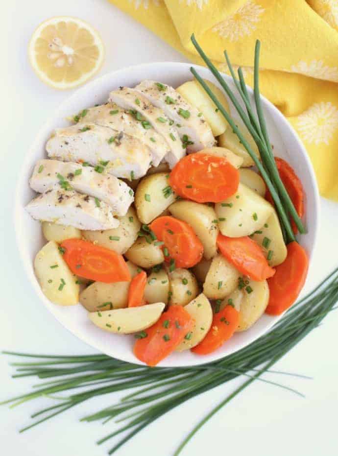 White bowl filled with sliced chicken breast, potatoes and carrots, with chives around the bowl