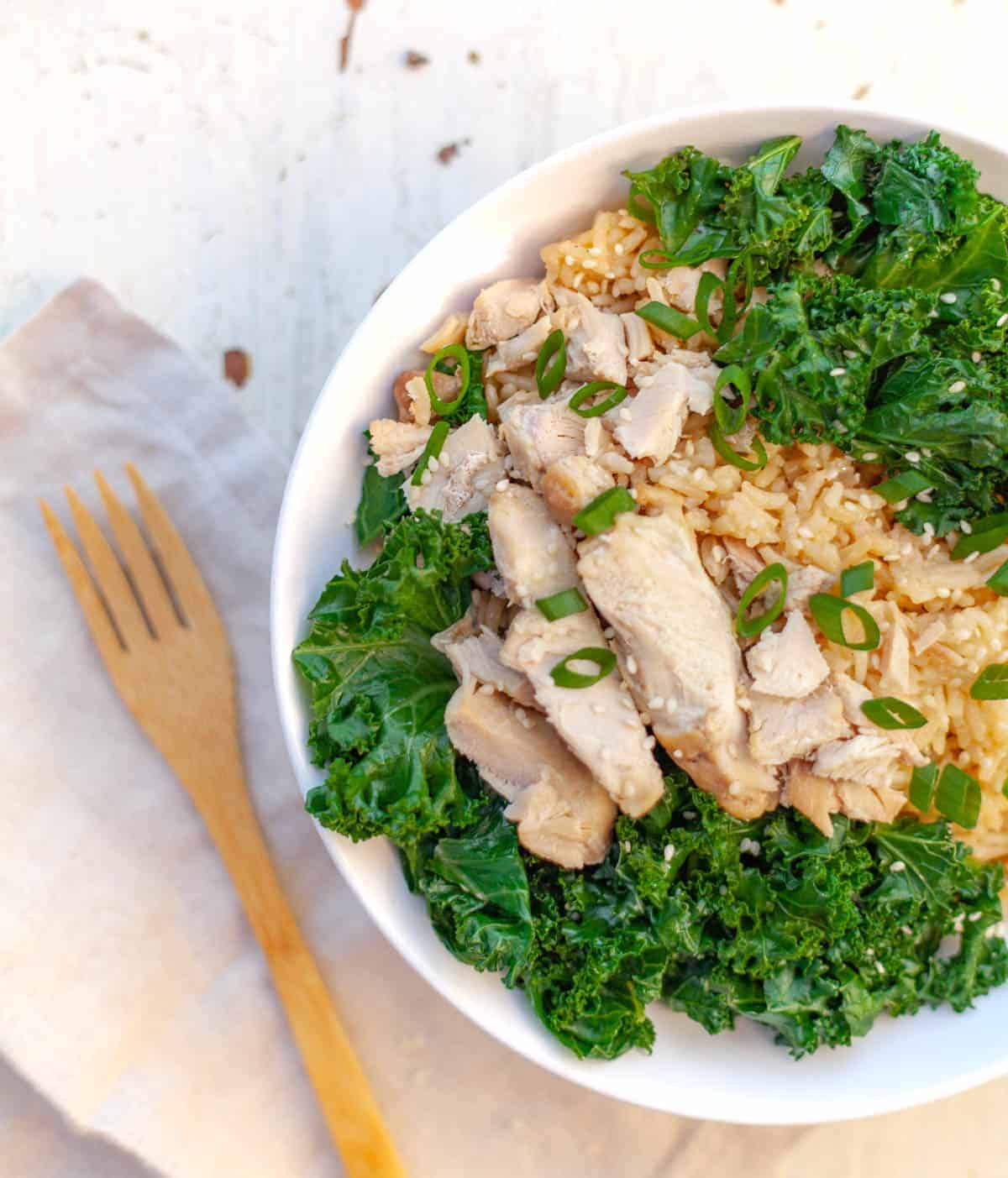 A white bowl filled with instant pot cooked brown rice and sliced chicken thigh with kale and green onion