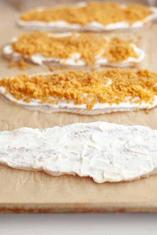 Sheet pan covered in parchment with raw fillets of cod topped with creme fraiche and panko