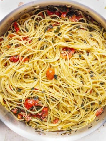 Skillet filled with cooked spaghetti noodles, tomatoes and kale sprinkled with parmesan cheese