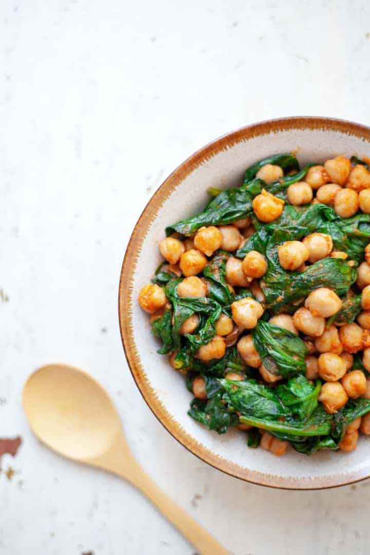 Brown bowl filled with chickpeas and spinach simmered in thick tomato sauce