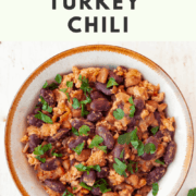 Bowl filled with turkey and bean chili garnished with parsley and a wooden spoon in front of the chili bowl