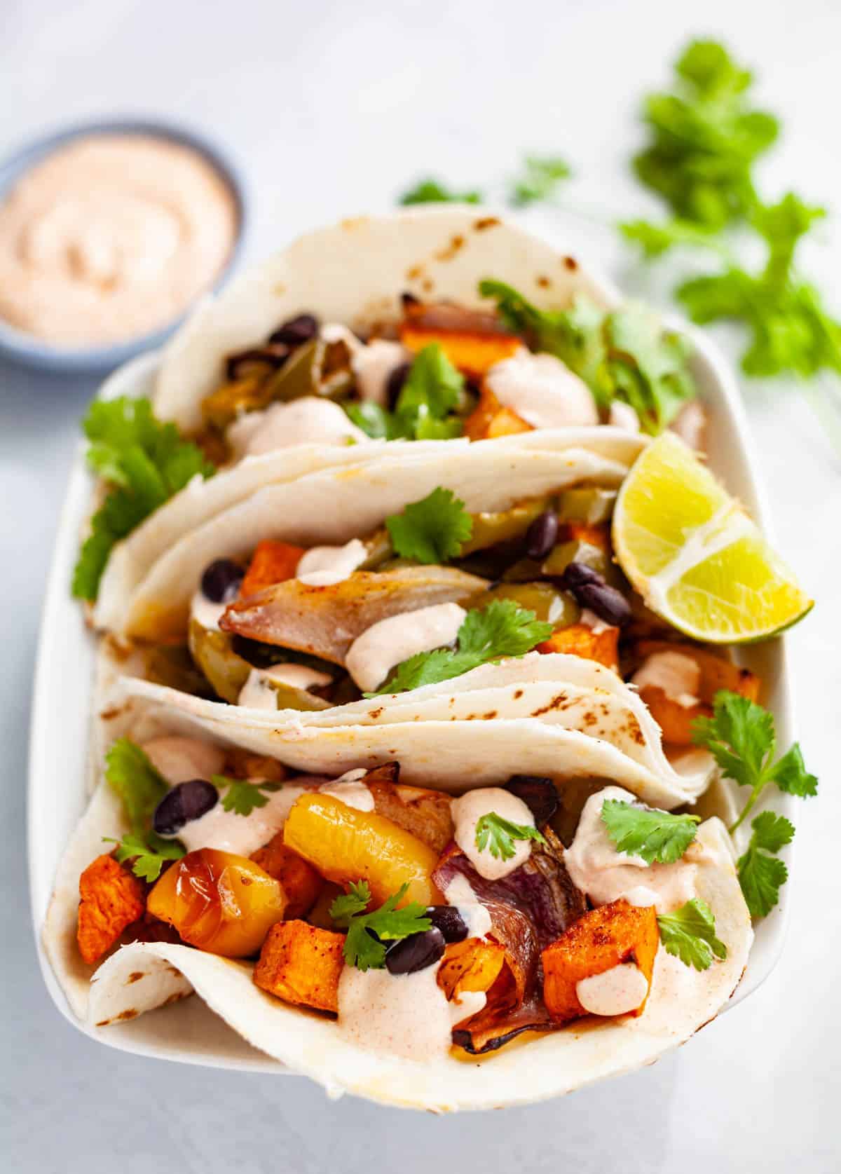 Three flour tortillas filled with vegetarian sweet potato fajitas and drizzled with smoky lime sour cream