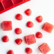 Red silicon ice cube tray next to red Frozen Watermelon and Coconut Water Ice Cubes in sea shell and square shapes