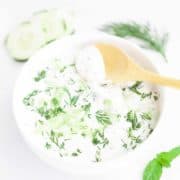 White bowl filled with cold yogurt sauce flavored with dill and grated cucumber