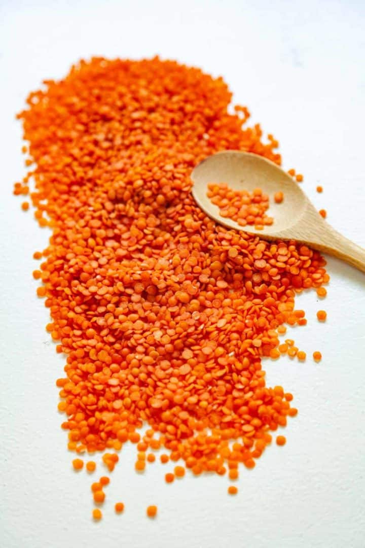 Uncooked red lentils on a white background with a small wooden spoon