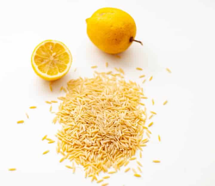 Uncooked orzo pasta on a white background in front of a lemon cut in half