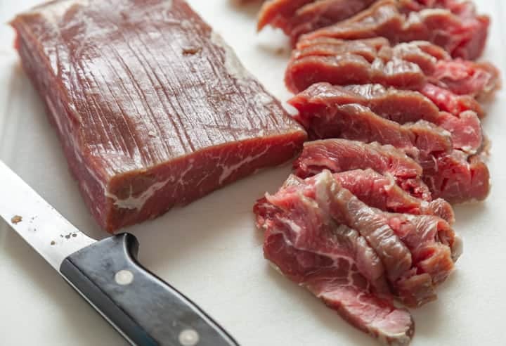 Thinly sliced raw flank steak on a cutting board