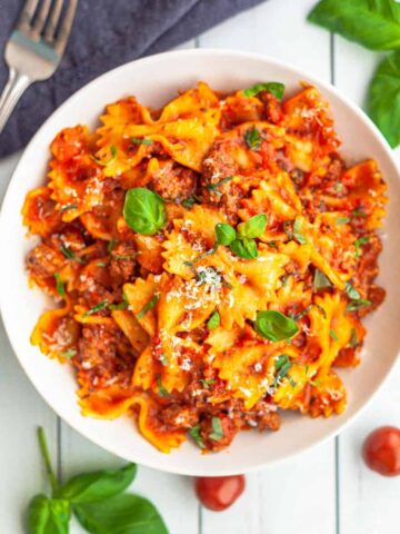 A white bowl filled with Instant Pot bowtie pasta cooked in a bolognese sauce topped with grated cheese and basil