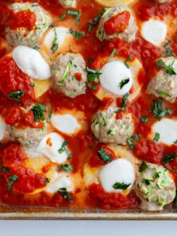 Sheet-pan of baked turkey and zucchini meatballs, rounds of polenta, melted mozzarella, tomato sauce and basil