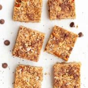Squares of granola bars made from almond butter, dark chocolate, coconut, pecans and chia seeds