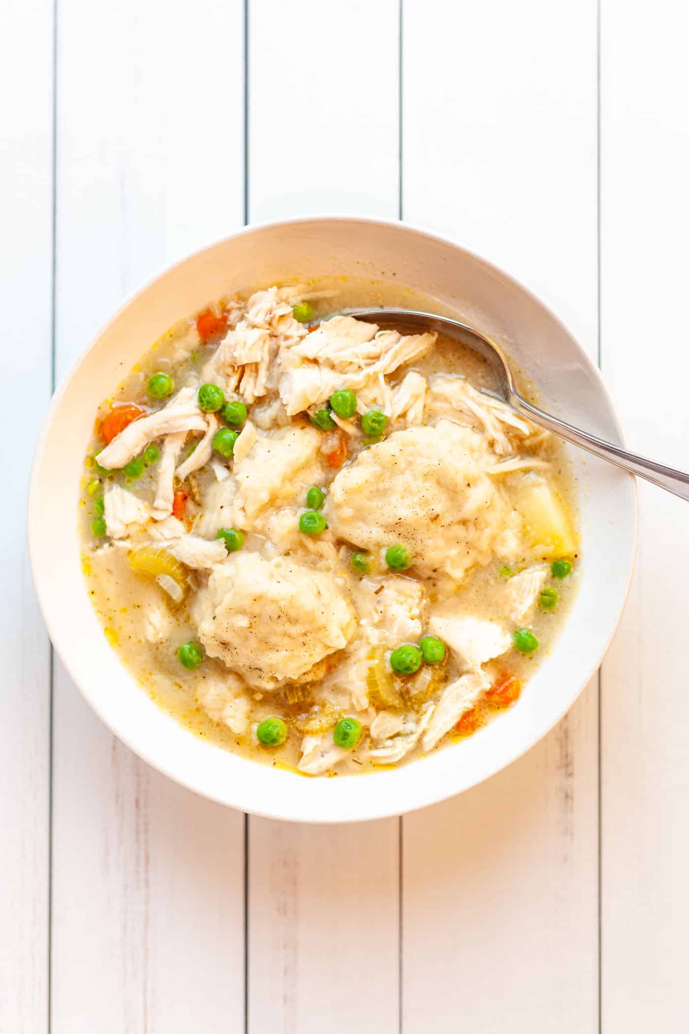 A bowl of shredded chicken breast, peas, carrots, potatoes and dumplings in broth