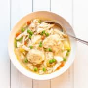 A bowl of shredded chicken breast, peas, carrots, potatoes and dumplings in broth