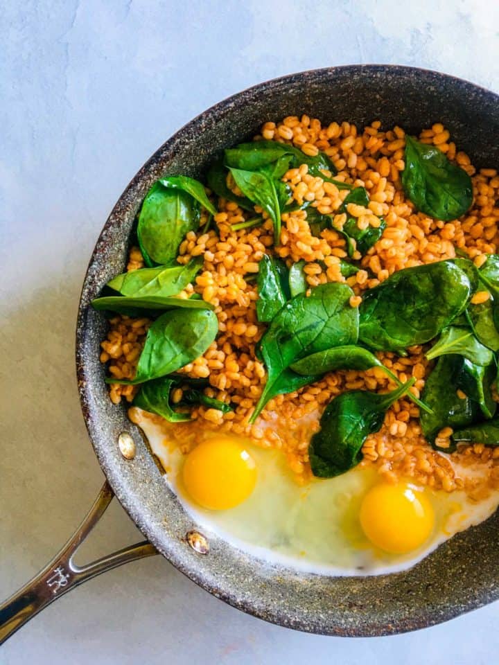 saute pan with barley, spinach and uncooked eggs