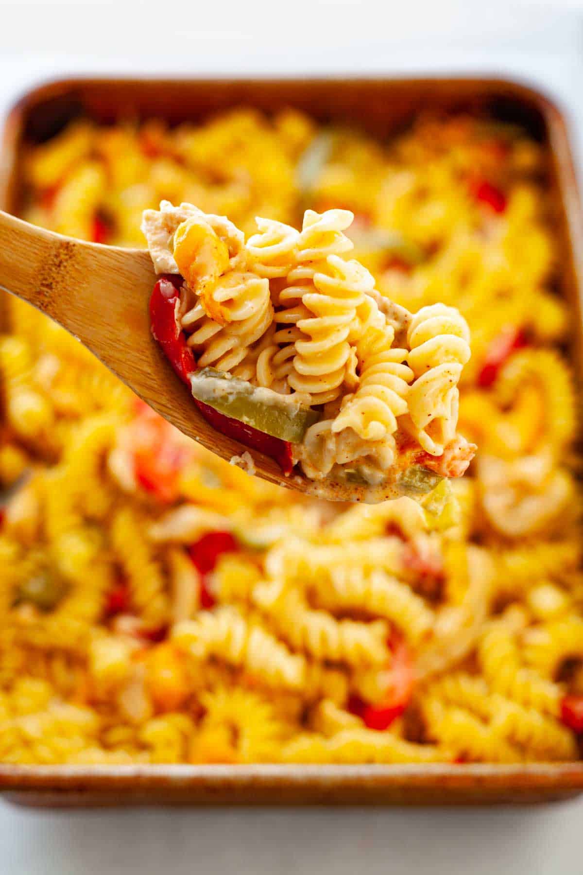 spoon with a scoop of cheesy rotini noodles with chicken and bell pepper