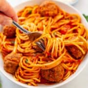 bowl of spaghetti twirled around a fork and meatballs in red sauce