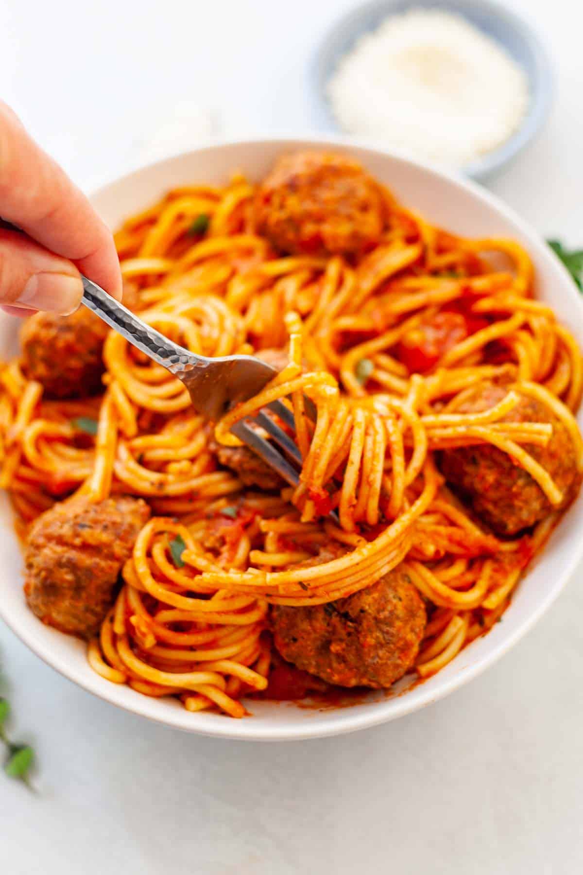 bowl of spaghetti twirled around a fork and meatballs in red sauce