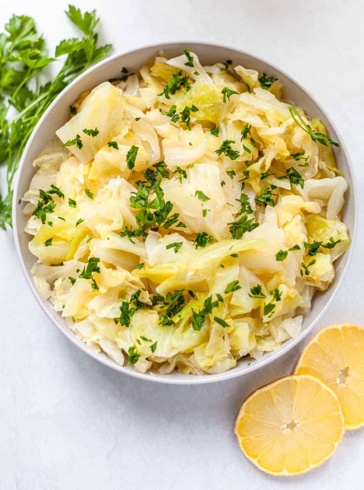 sliced cooked instant pot cabbage in a bowl topped with parsley with lemon slices on the side