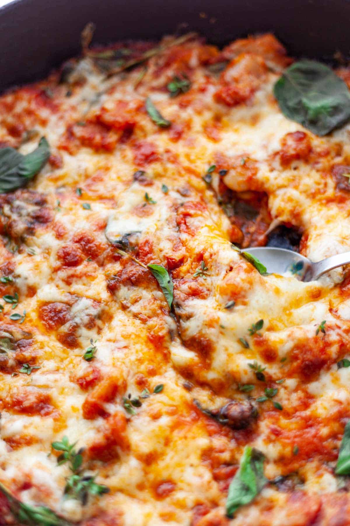 close-up of a spoon digging into a skillet of melted cheese and tomato sauce