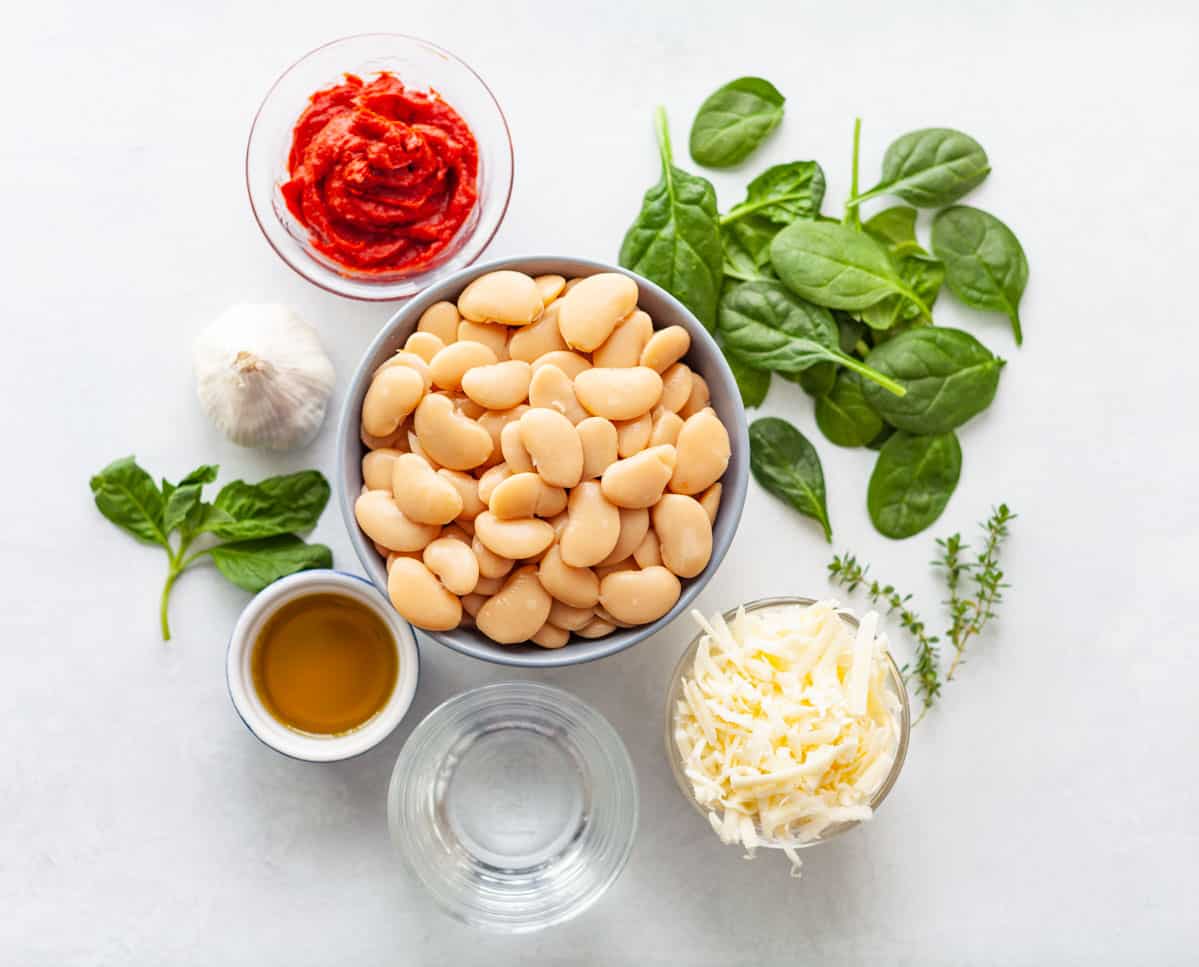 ingredients on a white background: canned butter beans, baby spinach, tomato paste, olive oil garlic, grated cheese and water