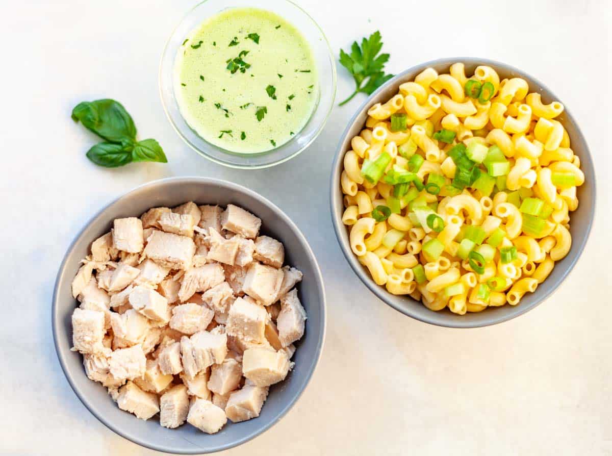 3 bowls of ingredients for macaroni and chicken salad: chopped chicken breast, cooked macaroni and green goddess dressing