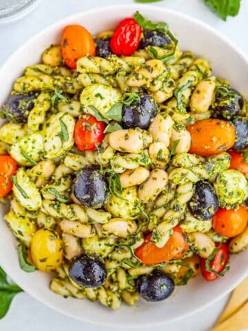 bowl of spinach pesto pasta salad with olive, tomatoes, mozzarella and beans