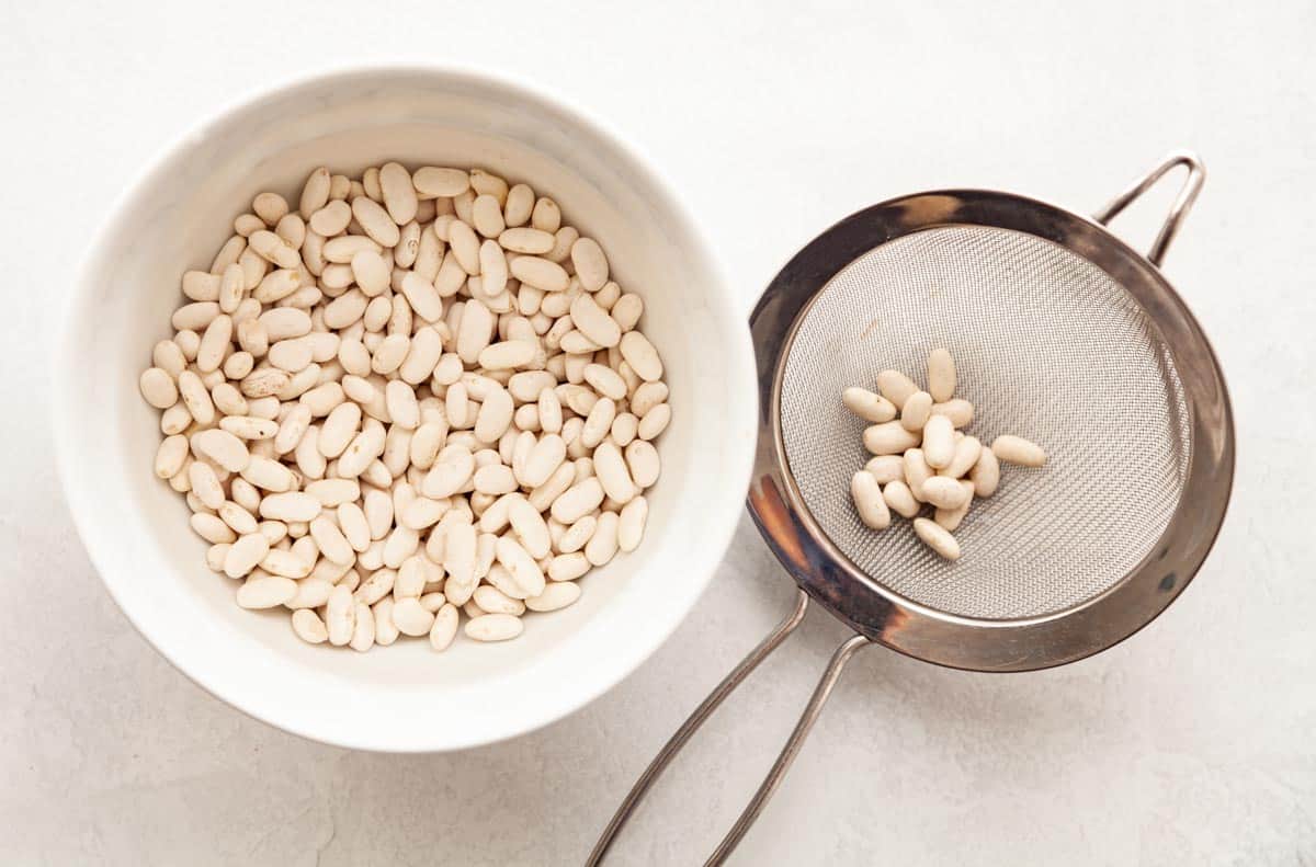 dried white beans in a bowl and fine mesh strainer