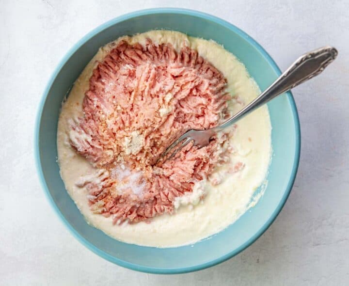 a bowl of raw ground turkey being mixed with ricotta an egg and breadcrumbs