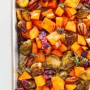 sheet pan of roasted sweet potatoes and Brussels sprouts garnished with pecans and dried cranberries
