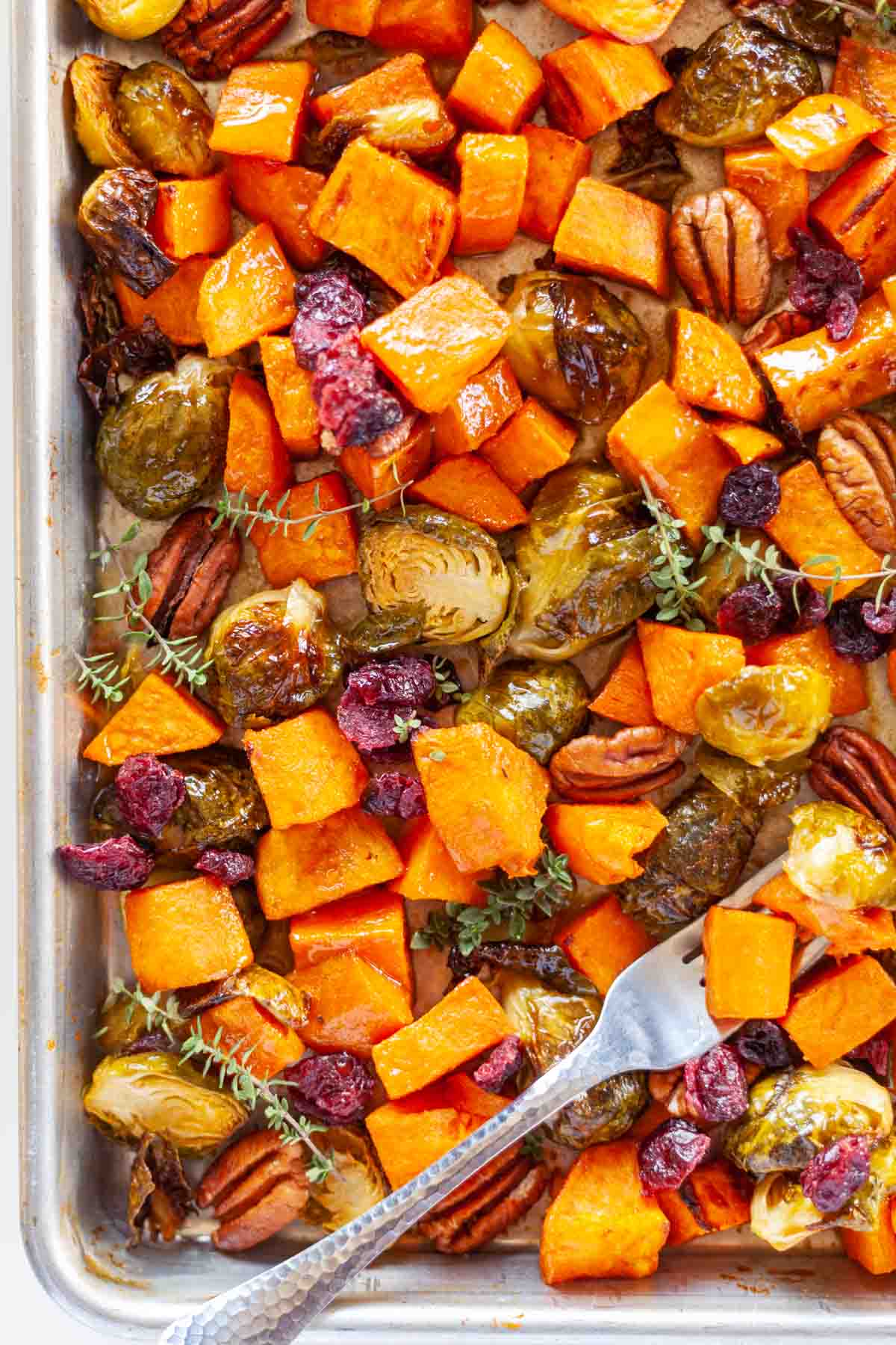 sheet pan of roasted sweet potatoes and Brussels sprouts garnished with pecans and dried cranberries