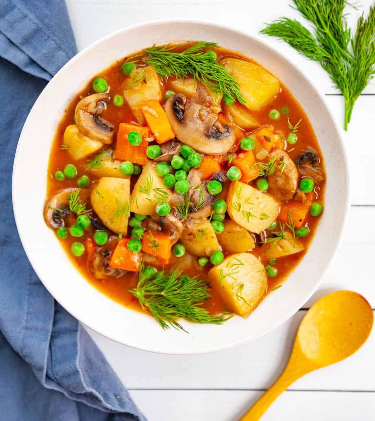 a bowl of vegetable stew made with potatoes, carrots and mushrooms garnished with dill