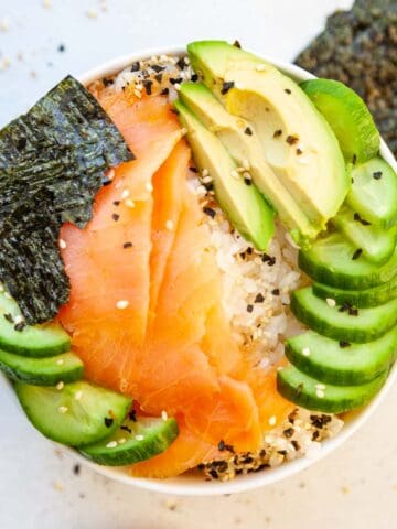 a bowl of salmon lox, seaweed, cucumber and white rice