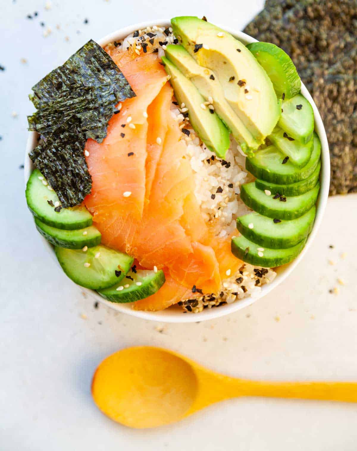 white rice bowl with salmon lox, cucumber, avocado and dried seaweed