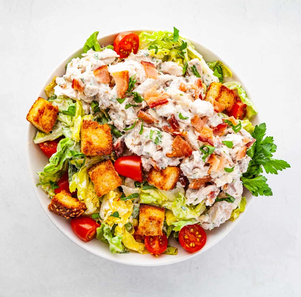 a bowl of chicken salad with greens and tomatoes