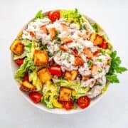 a bowl of chicken salad with greens and tomatoes