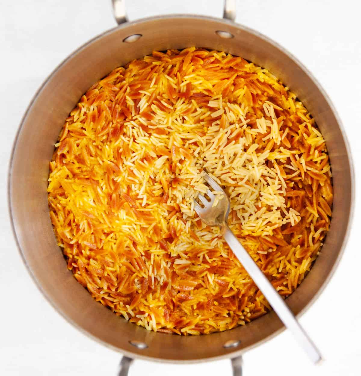 rice and orzo pilaf in a saucepan being fluffed with a fork