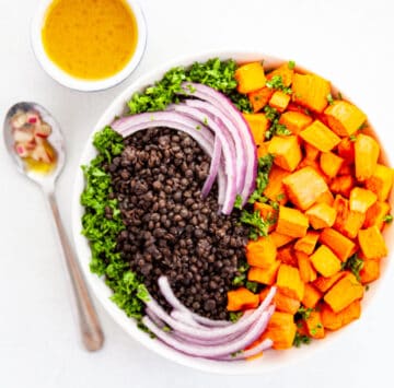 a bowl of black lentils, cubed sweet potatoes, sliced red onion and parsley with a small bowl of maple dijon dressing on the side