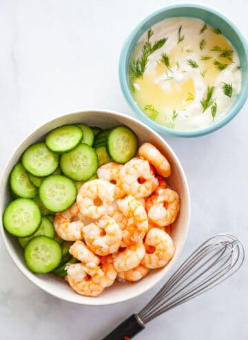 shrimp and cucumber in a bowl next to a creamy lemon salad dressing