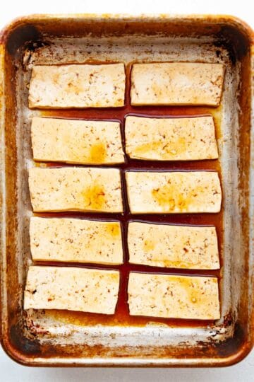 slices of uncooked tofu in a baking pan with sauce