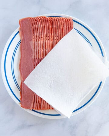 sliced raw turkey bacon on a plate with a paper towel