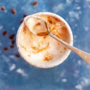 A mug of maple flavored coffee with foamy milk on top and a tiny stirring spoon filled with maple syrup.