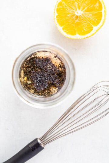 a jar of poppy seed salad dressing next to a whisk and cut lemon.