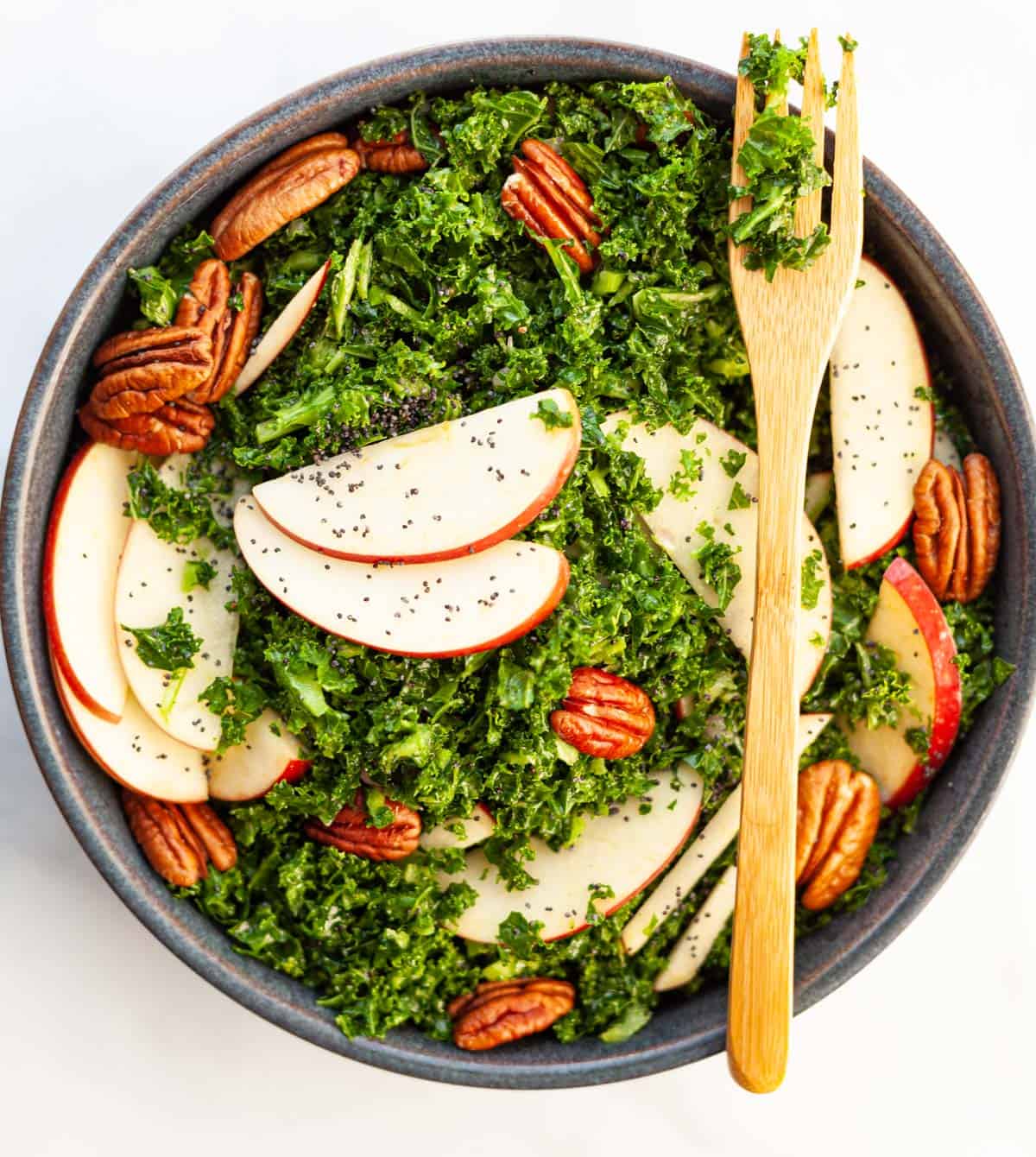 a bowl of kale slaw with sliced apples, pecans and poppy seeds