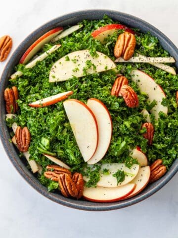 a bowl of kale slaw with sliced apples, pecans and poppy seeds