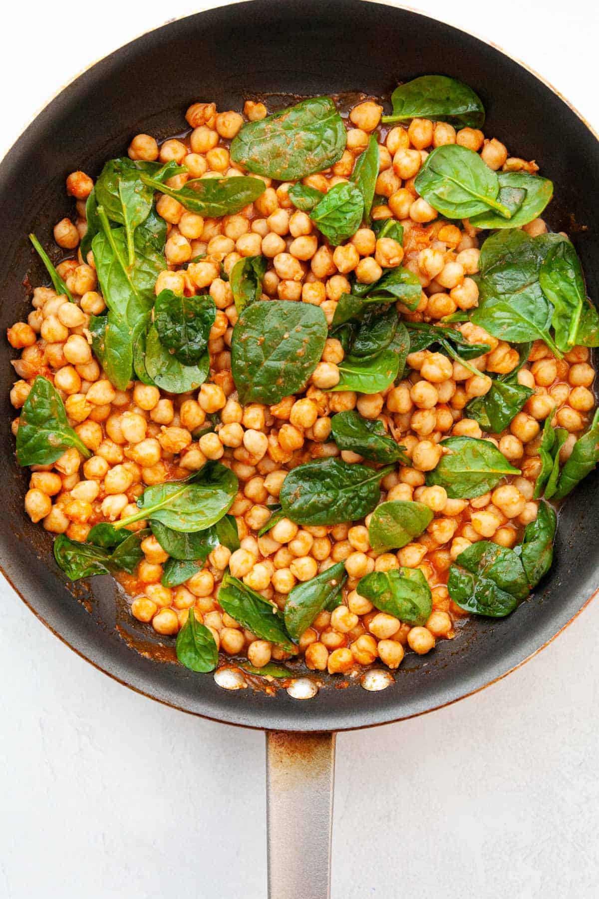 garbanzo beans in a skillet with baby spinach